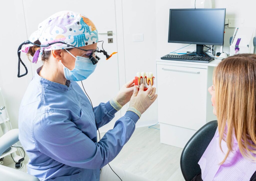 Dentist using a dental implant model to explain treatment options and factors that affect dental implant costs during a patient consultation.